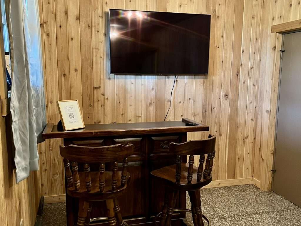 Lounge Suite at The Hidden Abbey with a wooden bar, two bar stools, and a mounted TV.